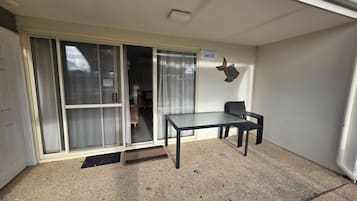 A room with a sliding glass door, a table with two chairs, and a sign indicating 'Jurien Bag Realty Unit 50'.