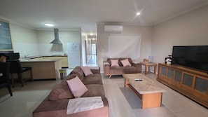 A living room with a sofa set, a coffee table, a TV, and a kitchen area with a stove and refrigerator.