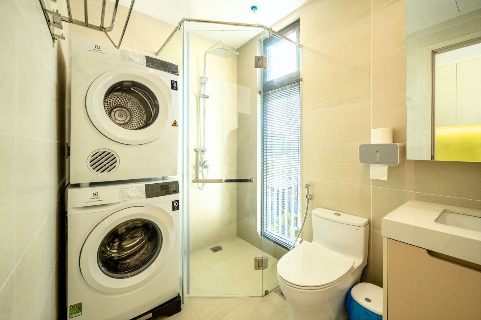 A compact bathroom with a washing machine, a toilet, and a glass-enclosed shower area.