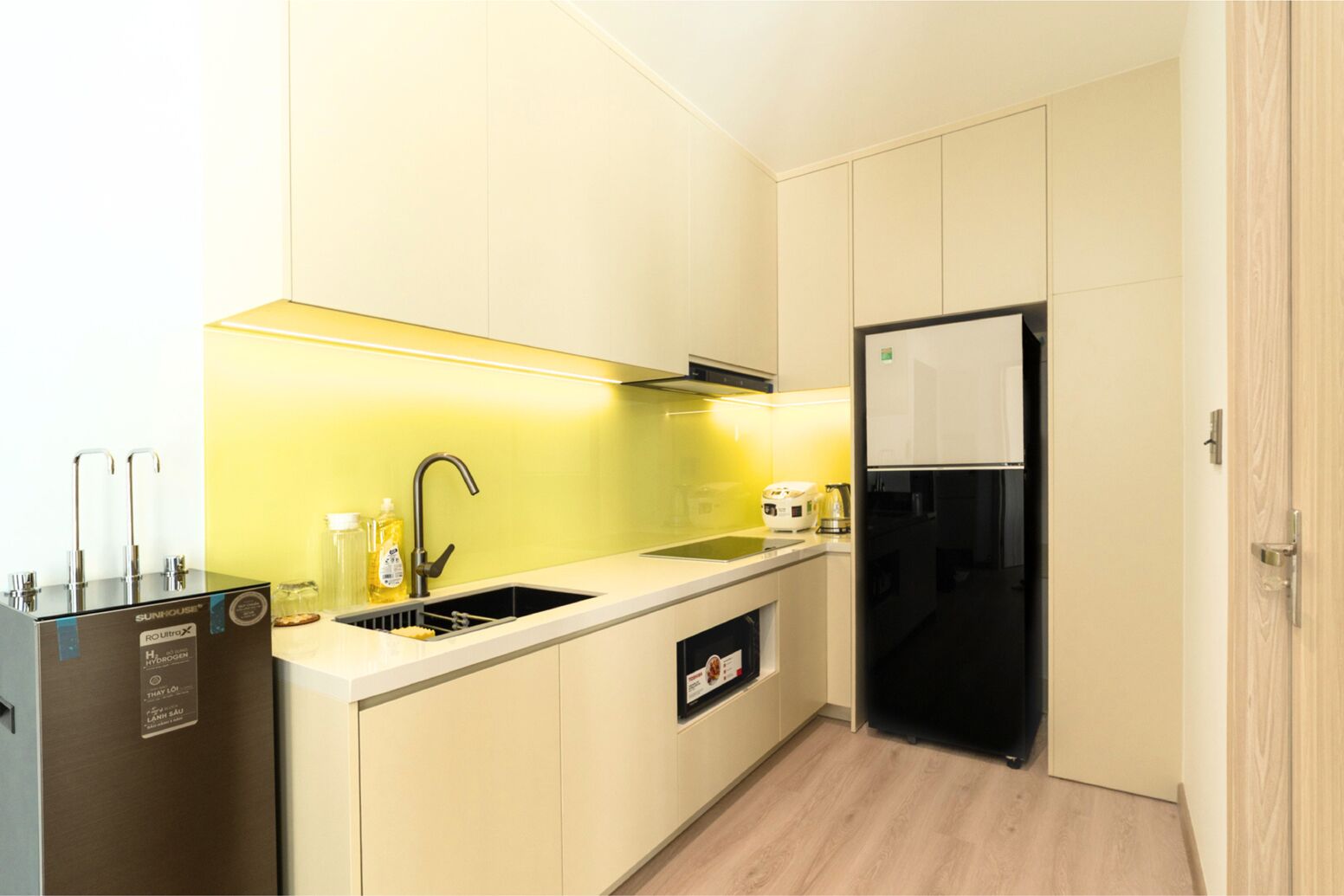 Una cocina moderna con lavavajillas integrado, un lavamanos con grifo y un refrigerador negro.
