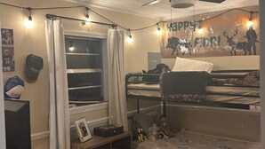 A bedroom with bunk beds, a ceiling fan, string lights, a window with curtains, and a birthday banner.