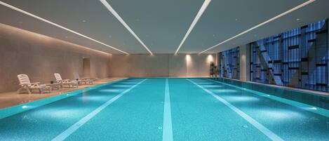 A large indoor swimming pool with clear lanes, lounge chairs, and a modern interior design.