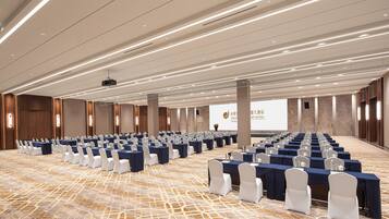 Una sala conferenze con file di tavoli e sedie, un proiettore e uno schermo con testo.