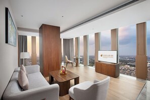 A modern hotel room with a large window, a flat-screen TV, a sofa, a coffee table, and a view of the cityscape. - Baoding Hotel of HangzhouGrandNewCentury (Hangzhou)