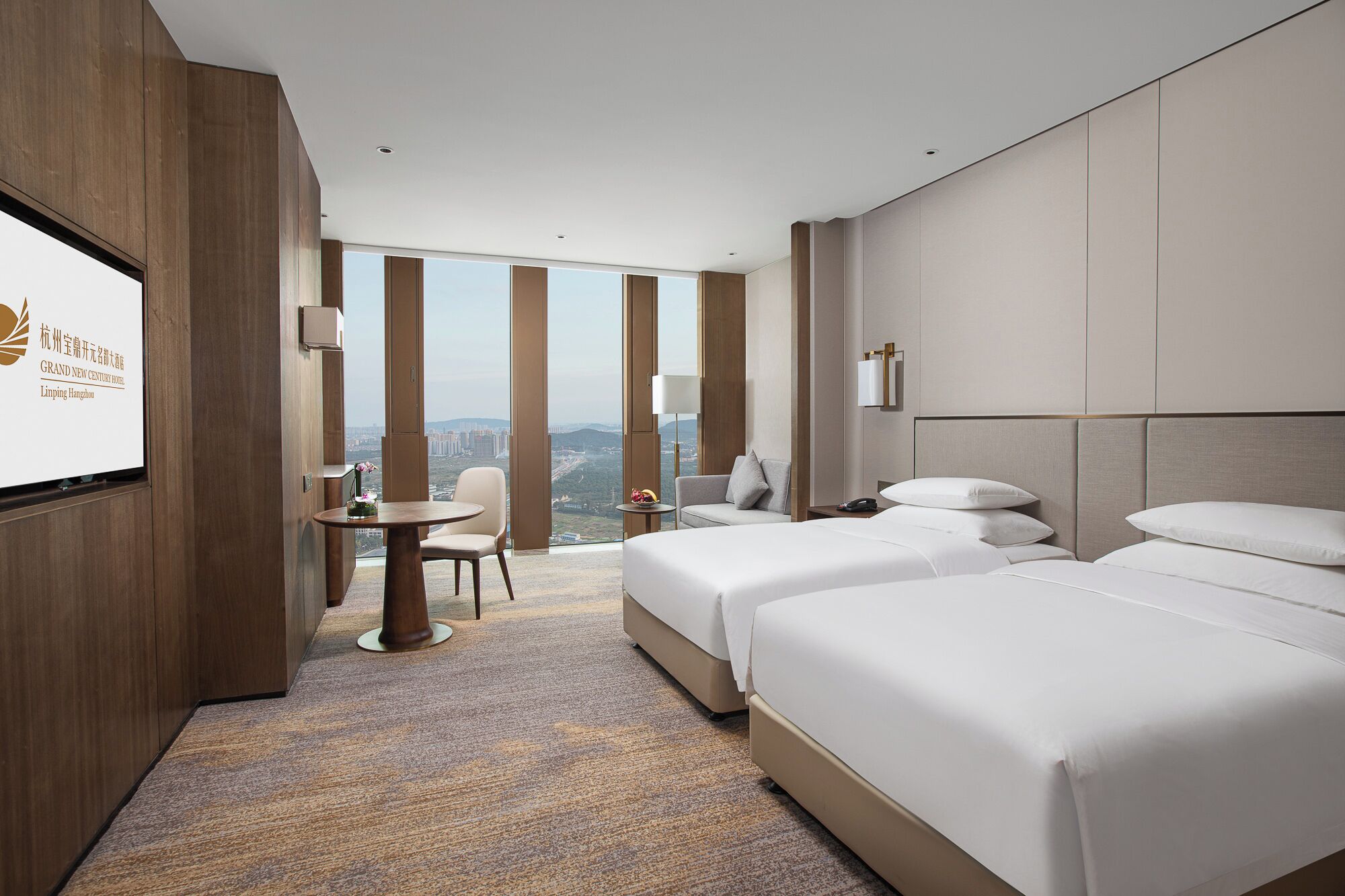A hotel room with two beds, a desk, and a view of the city.