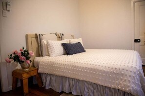 A bedroom with a bed, pillows, a bedside table with a vase of flowers, and a door.