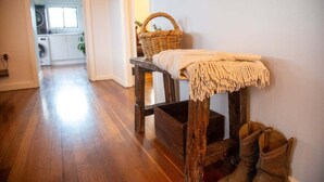 A hallway with a wooden bench, a basket, and a pair of boots. - The Farmhouse at Levenvale Farm (Bellingen)