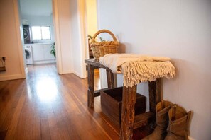 A hallway with a wooden bench, a basket, and a pair of boots. - The Farmhouse at Levenvale Farm (Bellingen)
