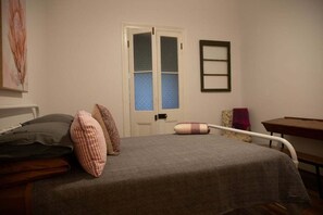 A bedroom with a bed, pillows, a chair, a table, and a door with a window. - The Farmhouse at Levenvale Farm (Bellingen)