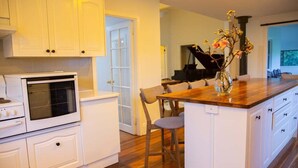 A kitchen with white cabinetry, a wooden countertop island, and a piano in the background. - The Farmhouse at Levenvale Farm (Bellingen)