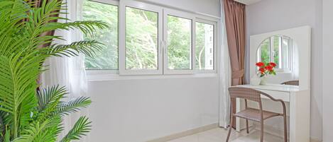 Une pièce avec une grande fenêtre, un bureau avec une chaise, un miroir et une plante en pot.