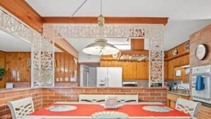 Uma sala de jantar com toalha de mesa vermelha, cadeiras brancas e parede de tijolos.