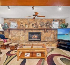 A living room with a stone fireplace, a ceiling fan, a television, and a coffee table. - Pet Friendly 3BR Home w/ Pool & Easy I75 Access (Valrico)
