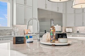 A modern kitchen with a marble countertop, a stainless steel faucet, and a decorative bottle. - Casa Elcoqui | LUX Gulf Views, Pool + Spa, Sleeps 16 (Panama City Beach)