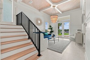 Una escalera con peldaños de madera y barandillas negras conduce a una sala de estar con un sofá azul, una mesa de centro y una araña.