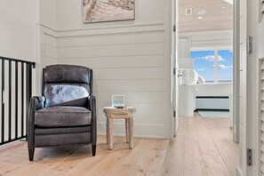 A room with a leather armchair, a small wooden table, and a view of the sky through an open door. - Casa Elcoqui | LUX Gulf Views, Pool + Spa, Sleeps 16 (Panama City Beach)