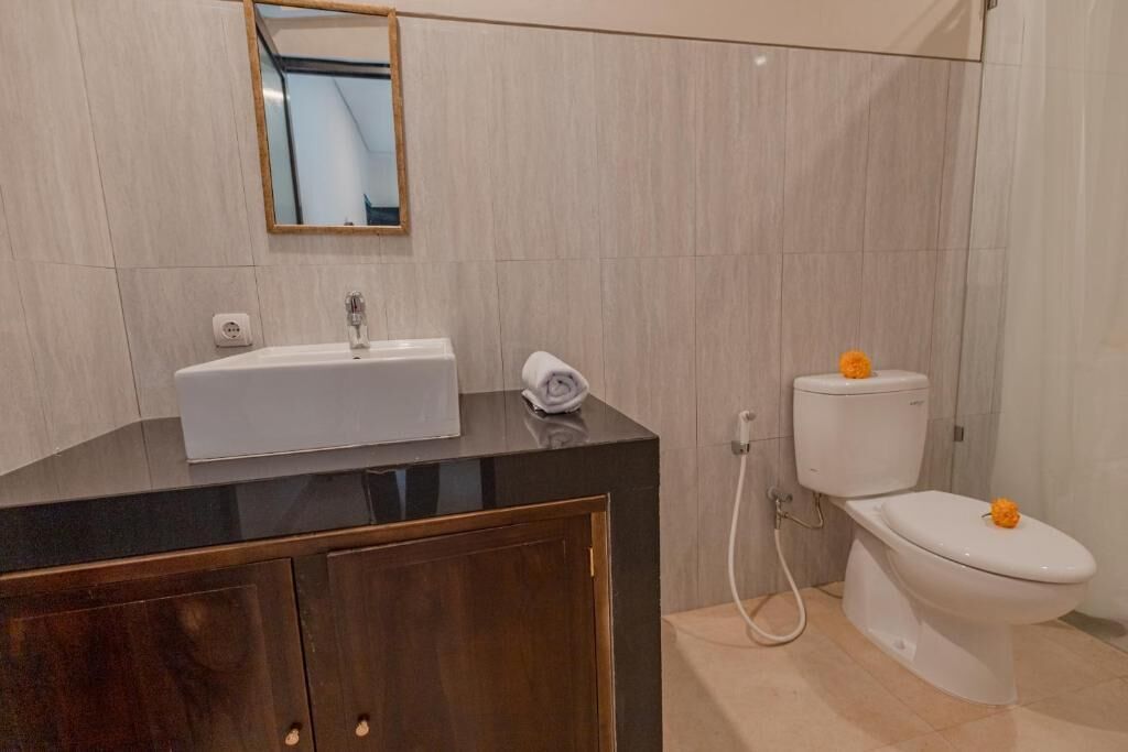 Un baño con lavamanos, espejo, inodoro y armario de madera.