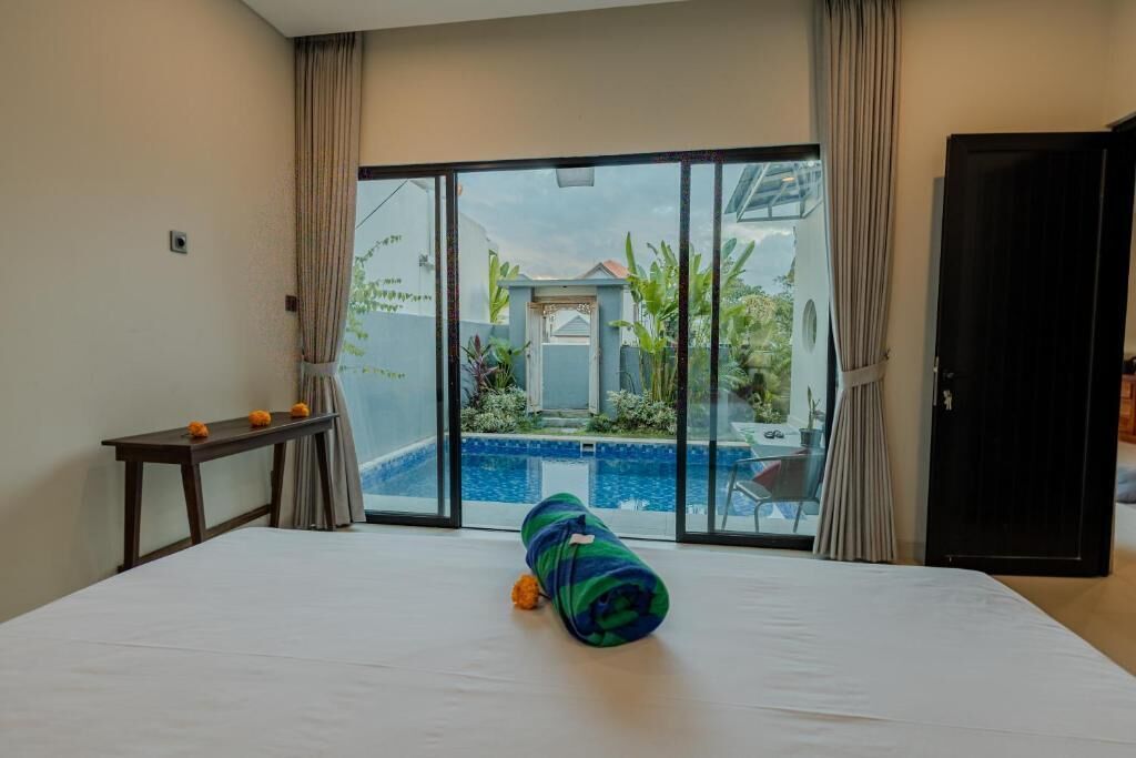 Habitación de hotel con una cama, una mesita con naranjas, un ventanal y vista a una piscina y zona exterior.