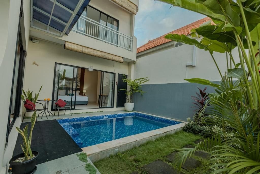 A two-story house with a swimming pool, outdoor furniture, and potted plants.