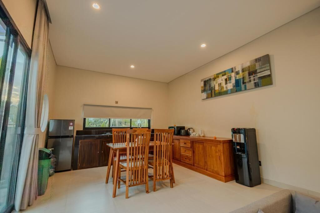A modern kitchen with wooden cabinets, a dining table with chairs, a refrigerator, and a window providing natural light.