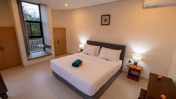 A hotel room with a large bed, bedside tables, a window with a view, and a ceiling-mounted air conditioner.
