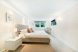 A bedroom with a bed, bedside table, lamp, and a desk with a chair. - Luxury Refurbished 3BR With Patio Kensington (London)