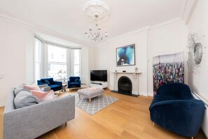 A living room with a fireplace, a television, and a large abstract painting. - Luxury Refurbished 3BR With Patio Kensington (London)