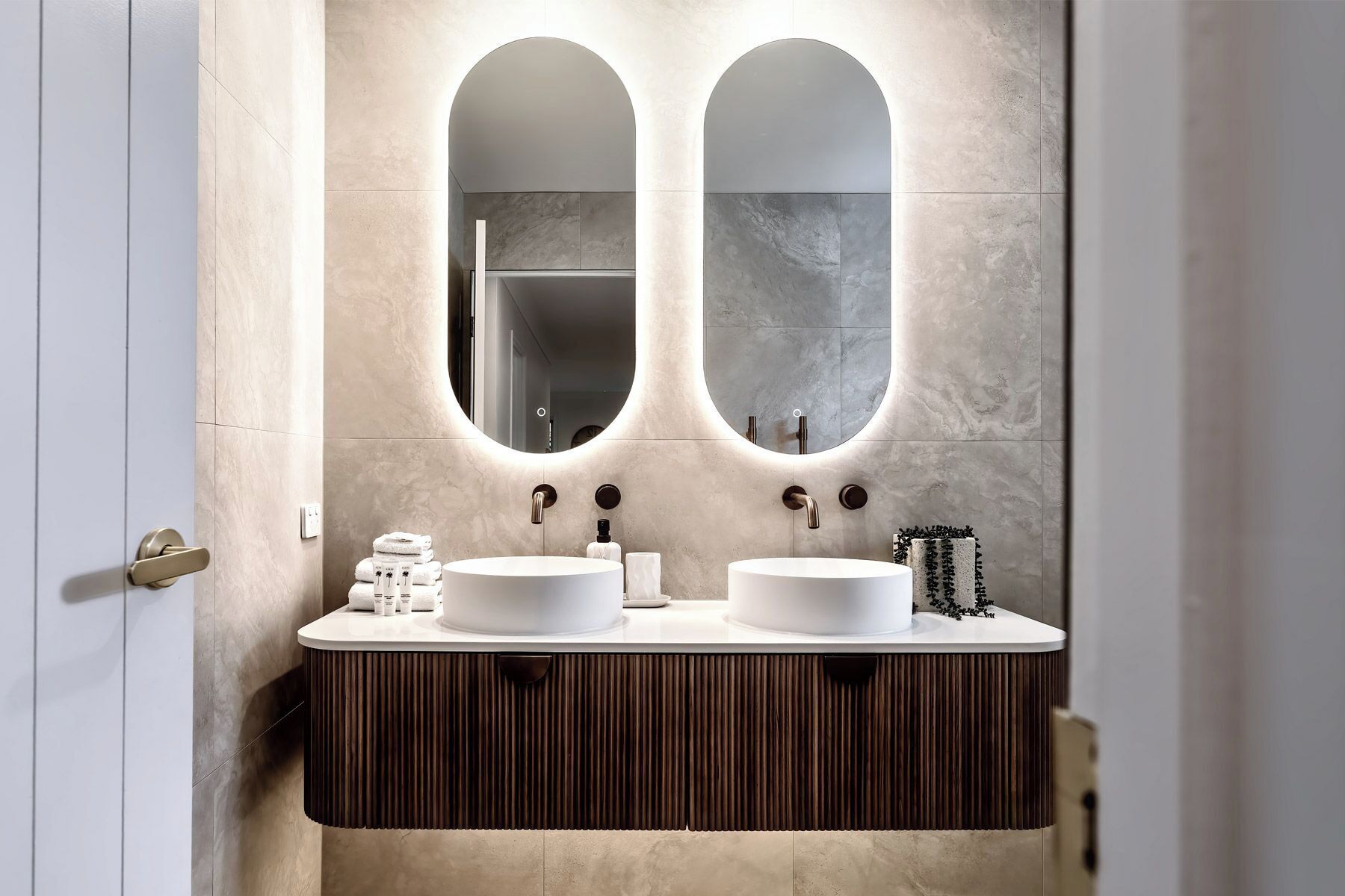 A bathroom with two oval mirrors, a double sink vanity, and a towel rack.
