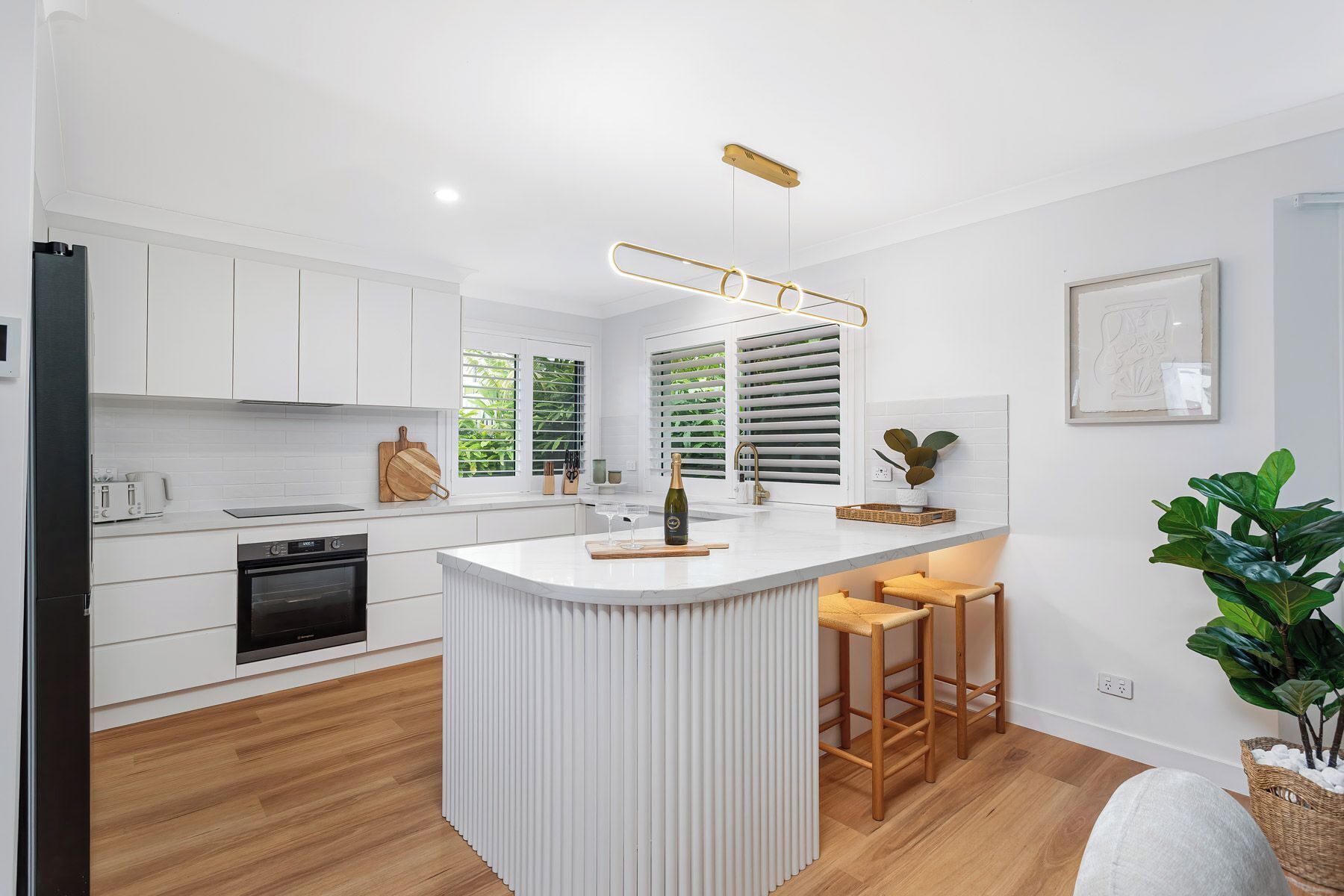 A modern kitchen with white cabinetry, a central island, and a wooden bar stool.