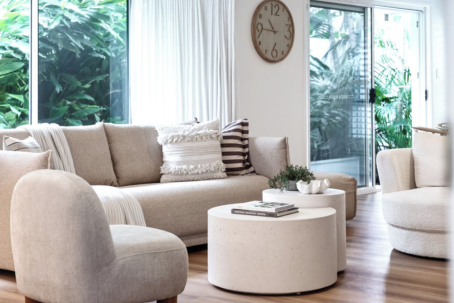 Un salon moderne avec un canapé, des fauteuils, une table basse et une horloge au mur.