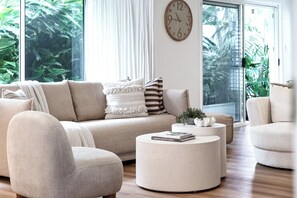 En moderne stue med sofa, lænestole, sofabord og et ur på væggen.