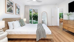 Ein Schlafzimmer mit Bett, Nachttischen, einem Spiegel, einem Deckenventilator und Blick ins Freie.
