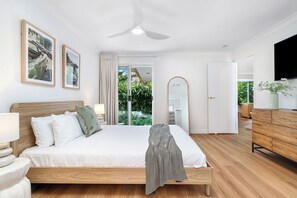 Ein Schlafzimmer mit Bett, Nachttischen, einem Spiegel, einem Deckenventilator und Blick ins Freie.