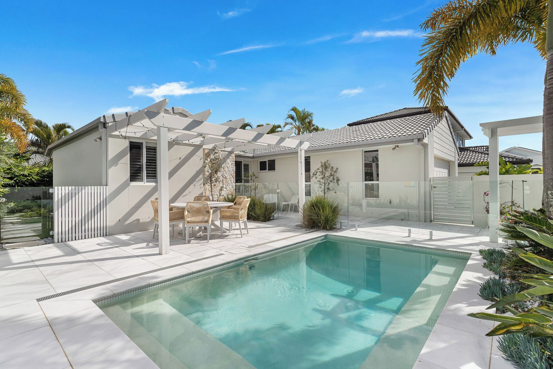 Una casa moderna con piscina, mobiliario exterior y una pérgola.