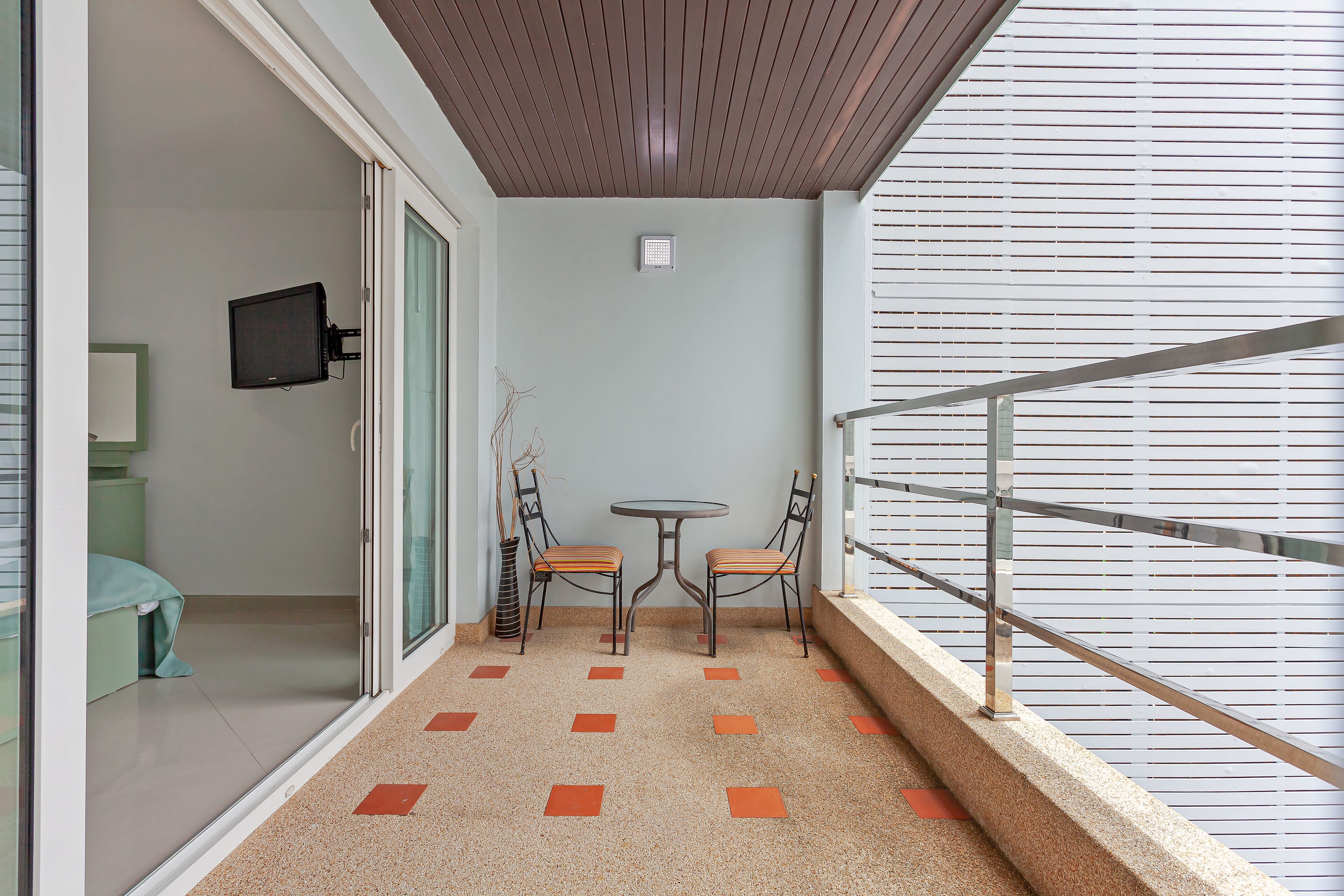 A balcony with a small table and two chairs, a television mounted on the wall, and a patterned floor.