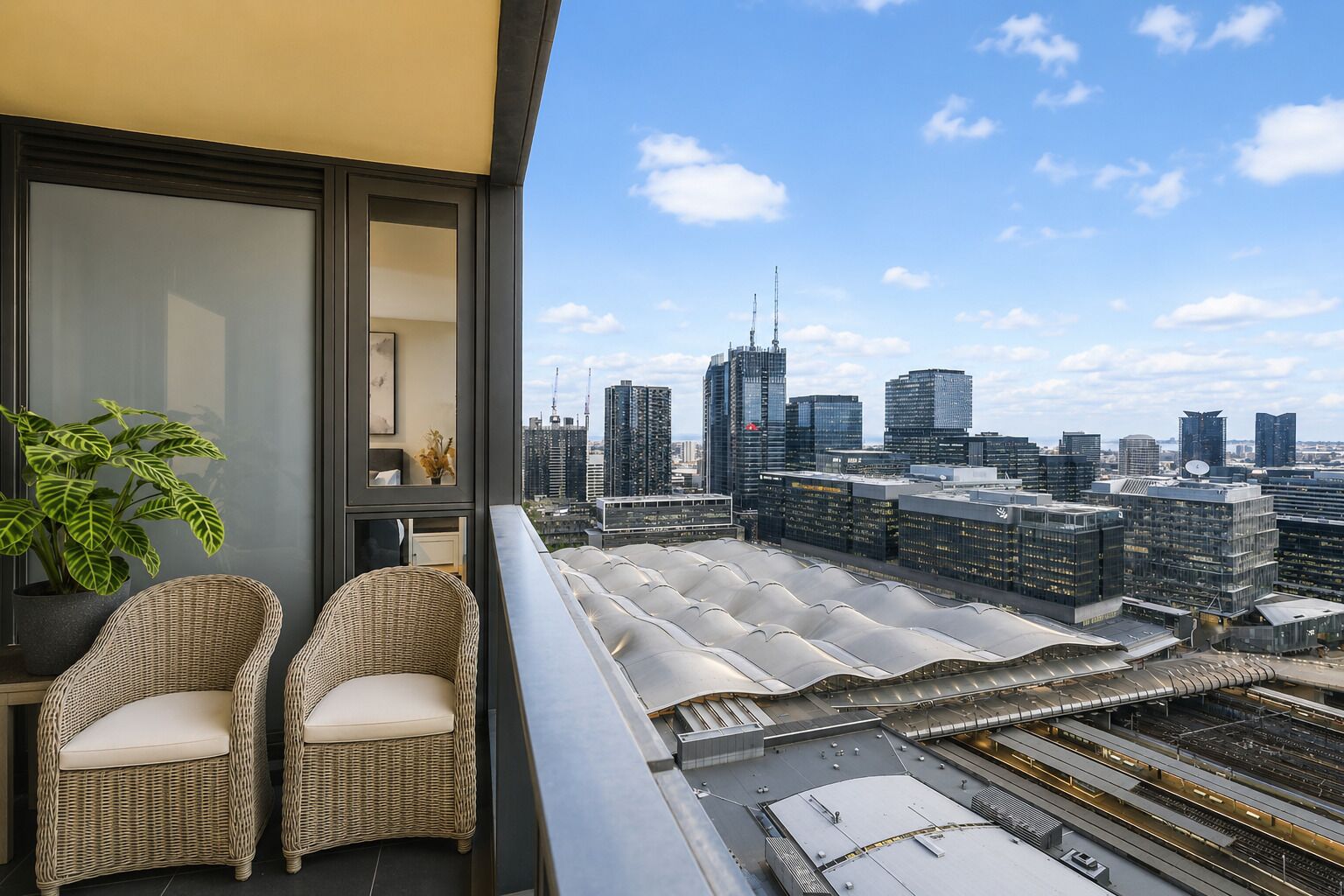 A balcony with wicker chairs, a potted plant, and a cityscape view.
