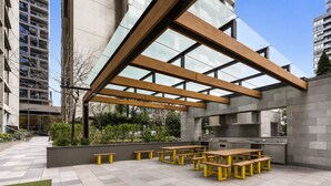 An outdoor patio with wooden benches and a modern kitchen area. - Upper West Side by Ready Set Stay (Melbourne)