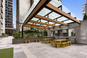 An outdoor patio with wooden benches and a modern kitchen area. - Upper West Side by Ready Set Stay (Melbourne)