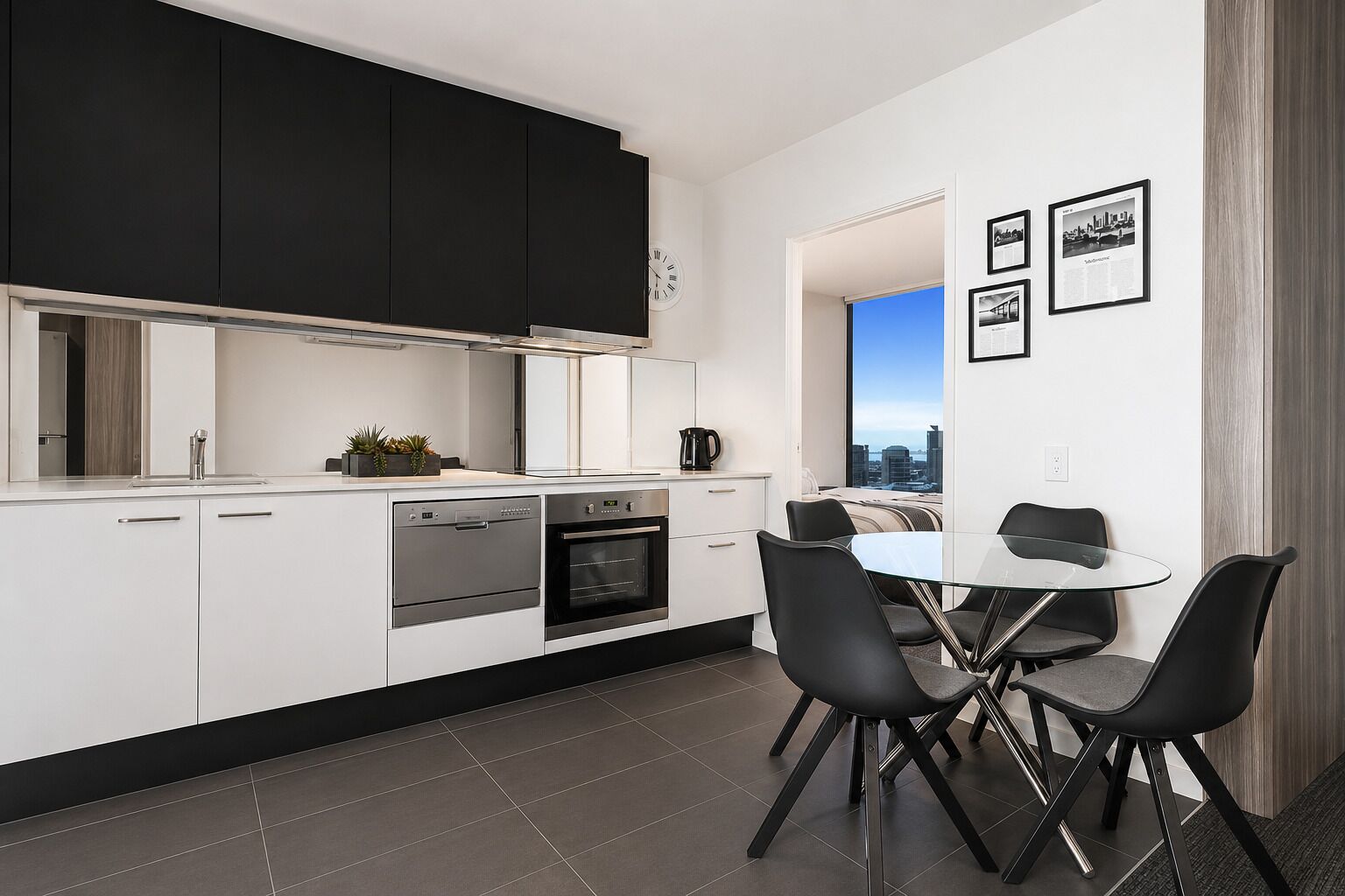 A modern kitchen with white cabinetry, a built-in oven, and a dining area with a glass table and black chairs.