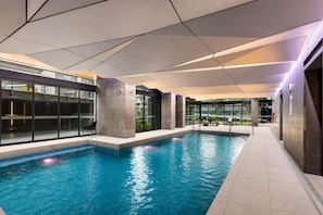 An indoor swimming pool with clear water, surrounded by modern architecture and glass walls. - Upper West Side by Ready Set Stay (Melbourne)