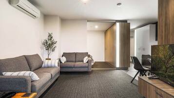 A modern living room with a sofa, a smaller couch, a coffee table, and a TV on a wooden cabinet.