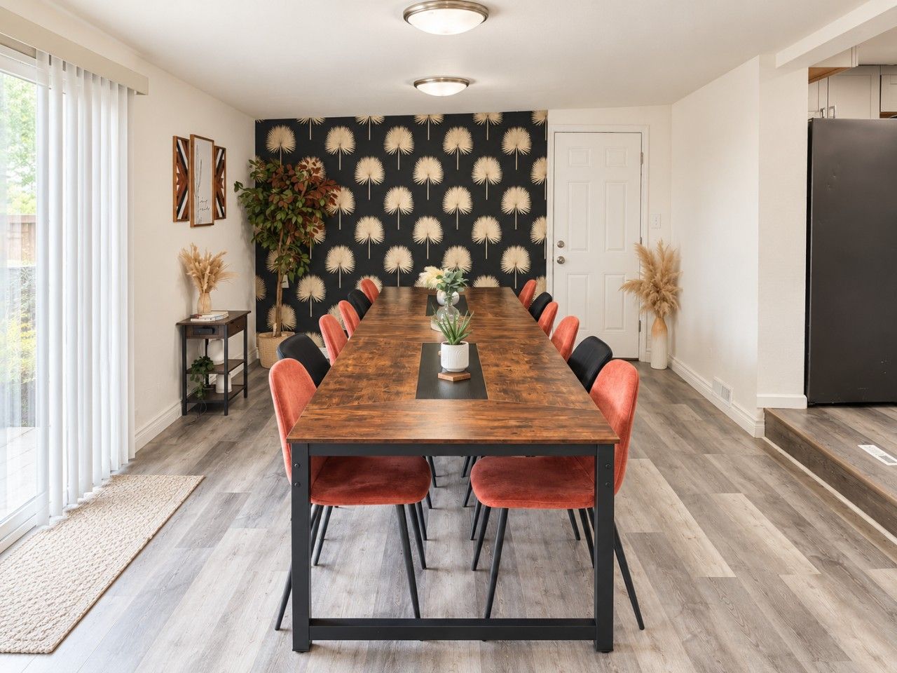 A dining room with a long wooden table, red chairs, and a black and white patterned wall.