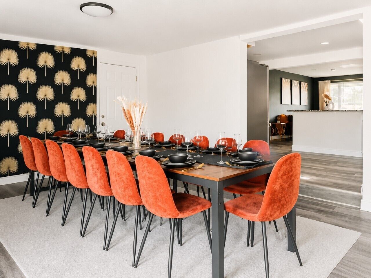 A modern dining area with a long table, orange chairs, and a black and gold wall decoration.