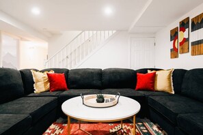 Ein modernes Wohnzimmer mit einem Ecksofa, einem runden Couchtisch und einer Treppe im Hintergrund.