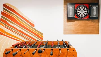 Ein Kicker, eine Dartscheibe und ein farbenfrohes, abstraktes Gemälde an der Wand.
