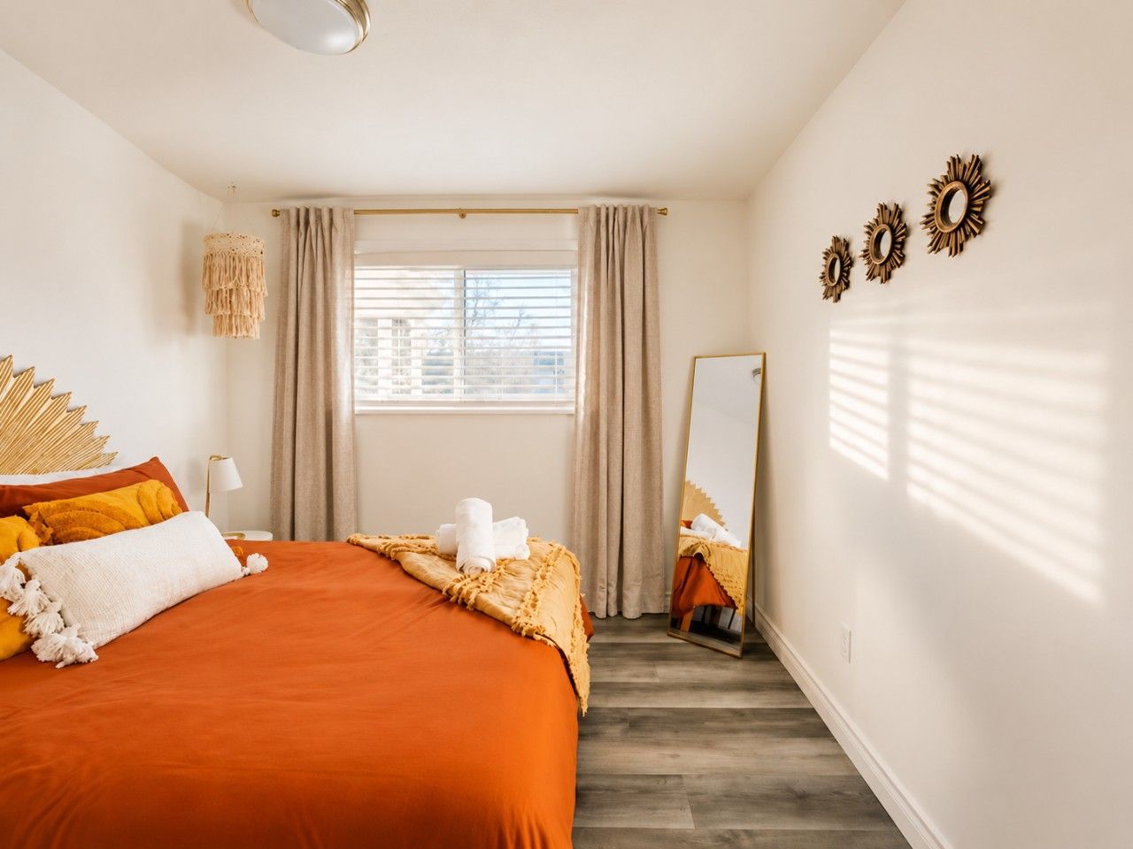 Een hotelkamer met een groot bed, een raam met gordijnen, een spiegel en decoratieve wandversiering.