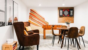 A modern room with a brown leather armchair, a round dining table with chairs, a dartboard, and a colorful abstract painting on the wall. - 5 BR | Hot Tub•Game Room•Fire Pit•Big Backyard (Westminster)
