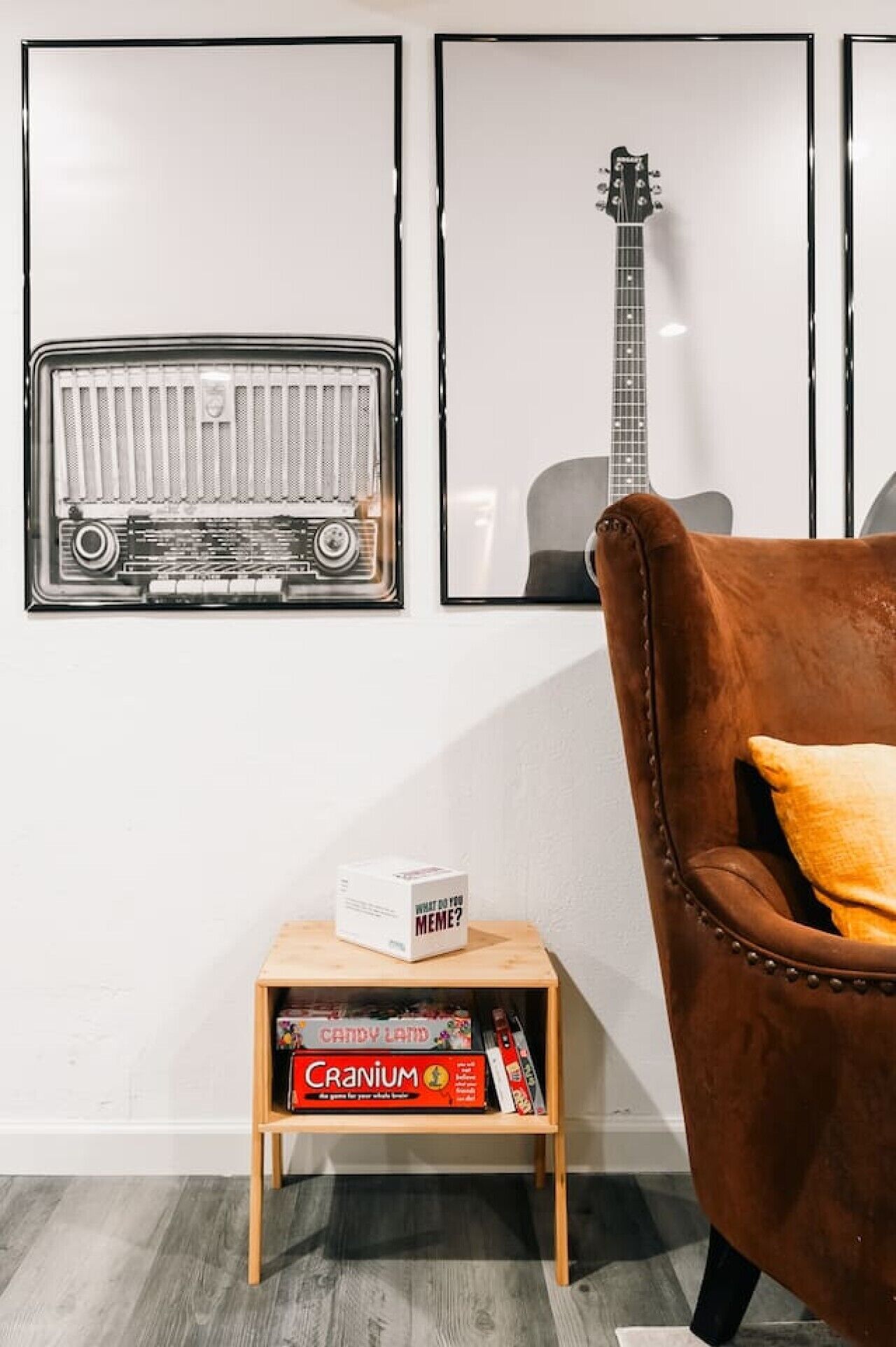 Quarto com uma poltrona de couro marrom, uma pequena mesa lateral de madeira com jogos de tabuleiro e duas fotos emolduradas na parede.