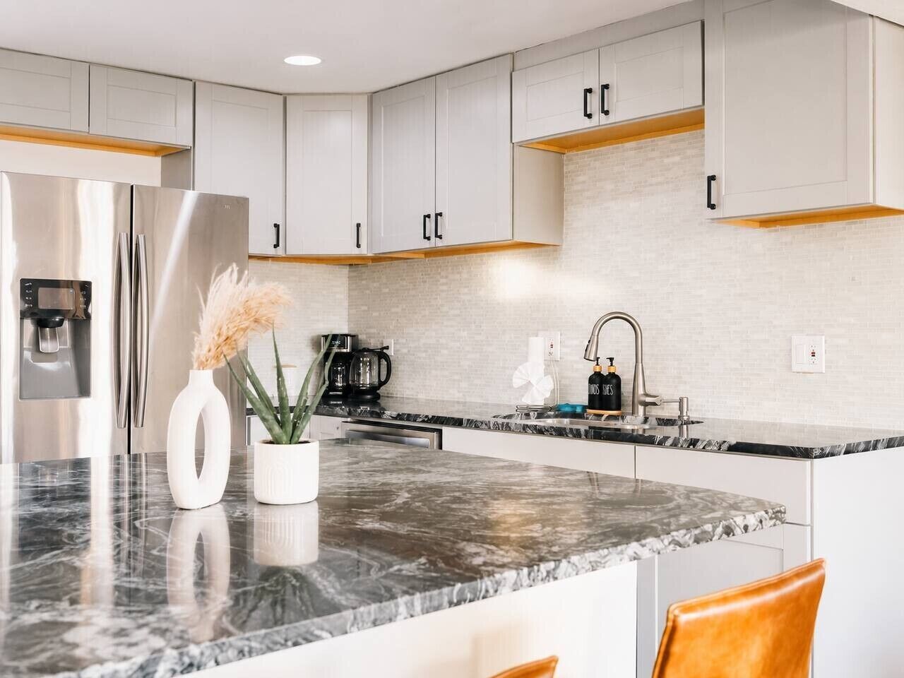 A modern kitchen with a stainless steel refrigerator, white cabinets, and a marble countertop.