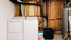 A laundry room with two front-loading washing machines, a water heater, and a water pump system. - 5 BR | Hot Tub•Game Room•Fire Pit•Big Backyard (Westminster)